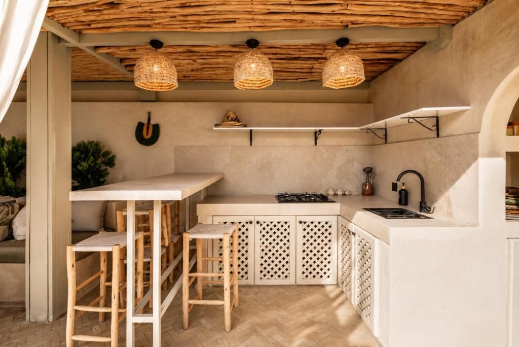A compact kitchen with a bar area, wooden stools, and a hanging light fixture.