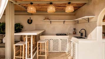 A compact kitchen with a bar area, wooden stools, and a hanging light fixture.