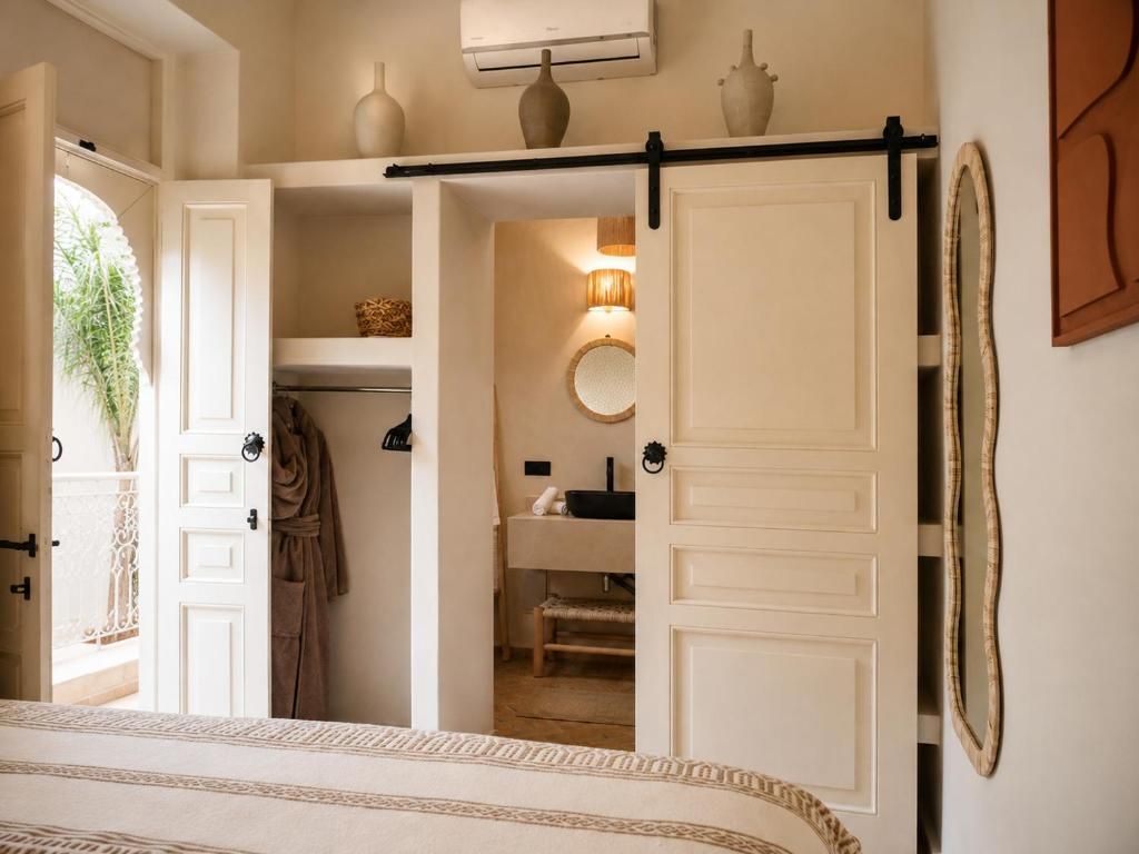 Un dormitorio con cama, armario, espejo y baño visible a través de una puerta abierta.