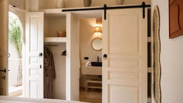 Un dormitorio con cama, armario, espejo y baño visible a través de una puerta abierta.