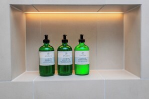 Tres botellas verdes de crema limpiadora y acondicionador Angan sobre una estantería.