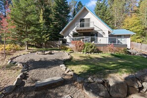 A two-story house with a balcony, surrounded by a natural landscape with trees and a rock garden. - Lakeview Retreat + Boat Slip & Waterfront Access (Coeur d'Alene)