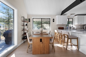 A modern kitchen with white cabinets, a wooden dining table, and a large window. - Lakeview Retreat + Boat Slip & Waterfront Access (Coeur d'Alene)