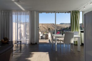 A modern living room with a large sliding glass door leading to a balcony with a view of a hilly landscape. - Holidays & Health in Finca Oasis - Apartamento 6 by Viilas Rivero (Telde)
