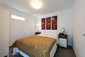 A hotel room with a bed, bedside tables, a lamp, a small cabinet, and artwork on the wall. - Holidays & Health in Finca Oasis - Apartamento 6 by Viilas Rivero (Telde)