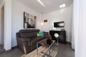 A modern living room with a brown leather sofa, a glass coffee table, a black entertainment unit, and a flat-screen TV. - Holidays & Health in Finca Oasis - Apartamento 6 by Viilas Rivero (Telde)