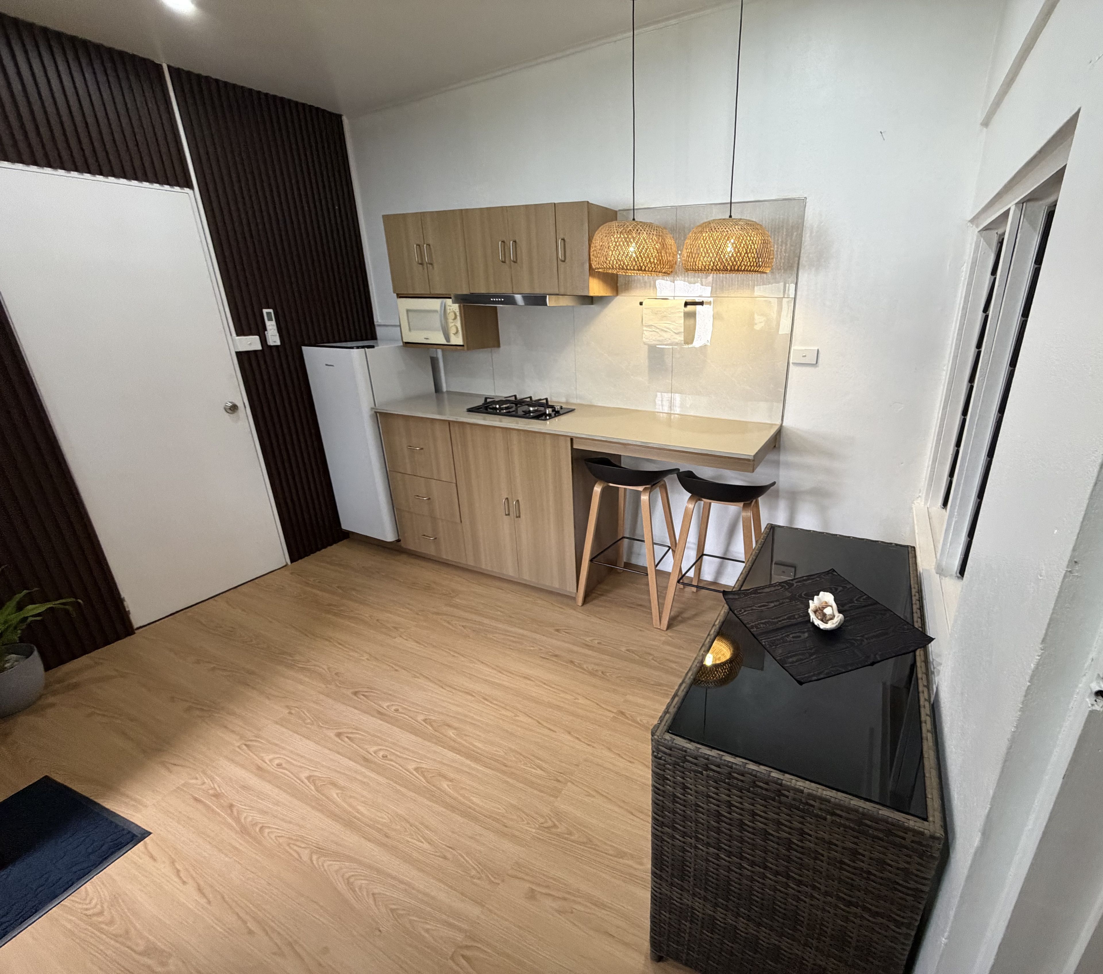 Cocina compacta con armarios de madera, un microondas, cocina a gas y dos taburetes de bar.