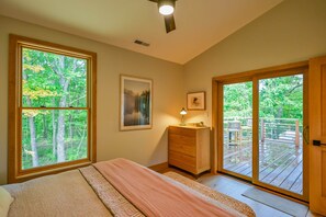 A bedroom with a bed, a dresser, a nightstand, a lamp, and a window with a view of trees. - Ramblewood Lodging 5 (Athens)