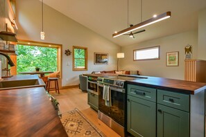 A modern kitchen with a central island, built-in oven, and a large window providing a view of greenery. - Ramblewood Lodging 5 (Athens)