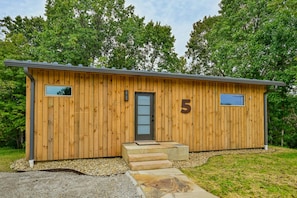 A wooden cabin with a number '5' on the door, a small window, and a set of steps leading to the entrance. - Ramblewood Lodging 5 (Athens)