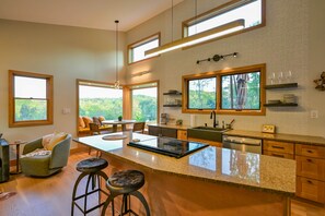 A modern kitchen with a central island, bar stools, and large windows offering views of the outdoors. - Ramblewood Lodging 4 (Athens Township)