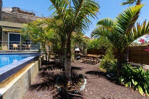 A pool area with a tiled edge, surrounded by palm trees and a wooden deck. -  Jardines del Cura - Apartamento 4 by Villas Rivero (Mogán)