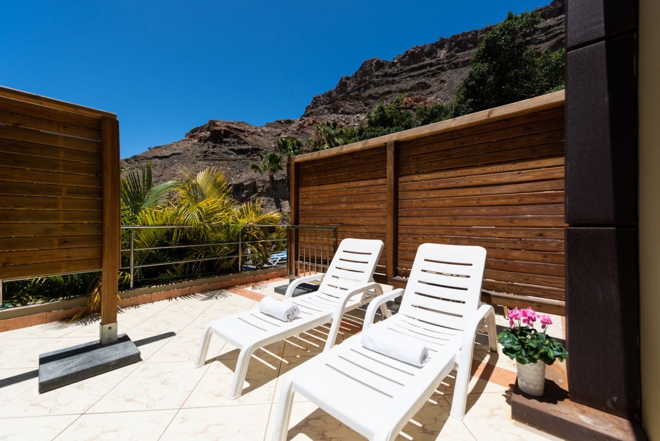 Una terraza con sillones blancos, un cerco de madera y vistas a un paisaje montañoso.