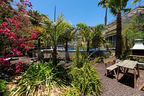 A pool area with palm trees, a wooden bench, and a table. -  Jardines del Cura - Apartamento 4 by Villas Rivero (Mogán)