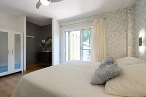 Ein Schlafzimmer mit einem großen Bett, einem Deckenventilator, einem Fenster mit Vorhängen und Blick ins Freie.