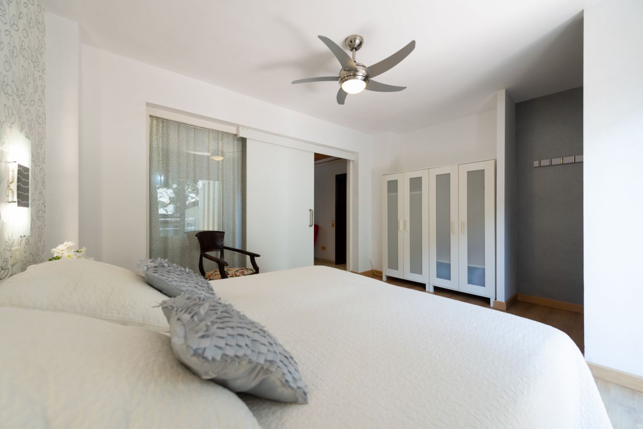 Un dormitorio con una cama grande, un ventilador de techo, un armario y una ventana con cortinas.