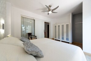 Un dormitorio con una cama grande, un ventilador de techo, un armario y una ventana con cortinas.