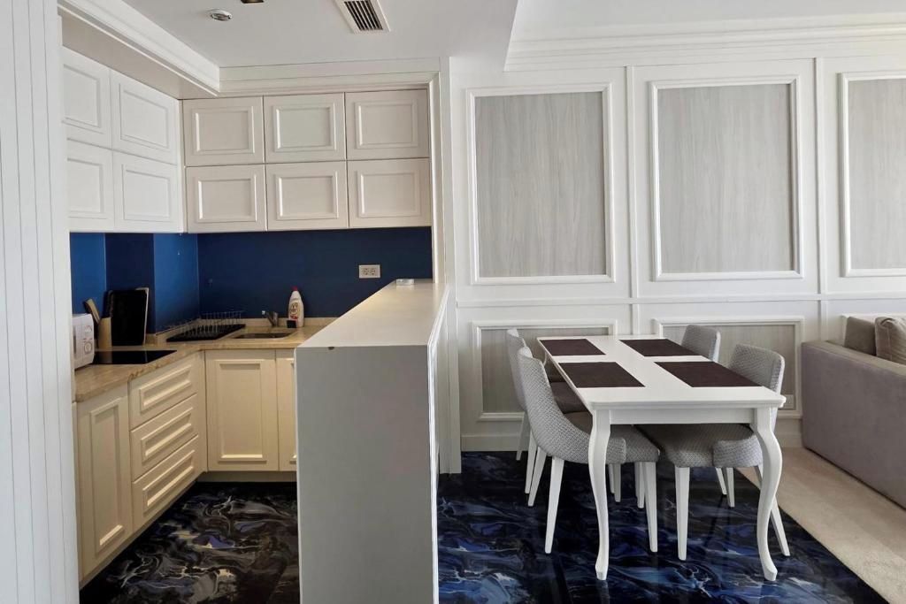 Une cuisine compacte avec des meubles blancs, un pare-feu bleu et un coin repas comprenant une table et des chaises blanches.