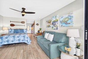 Ein Schlafzimmer mit einem Bett, einem Deckenventilator, einem blauen Sofa und Kunstwerken an den Wänden.