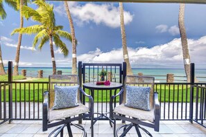 Eine Terrasse mit zwei Stühlen und einem Tisch mit Blick auf einen Strand, an dem Palmen und das Meer zu sehen sind.
