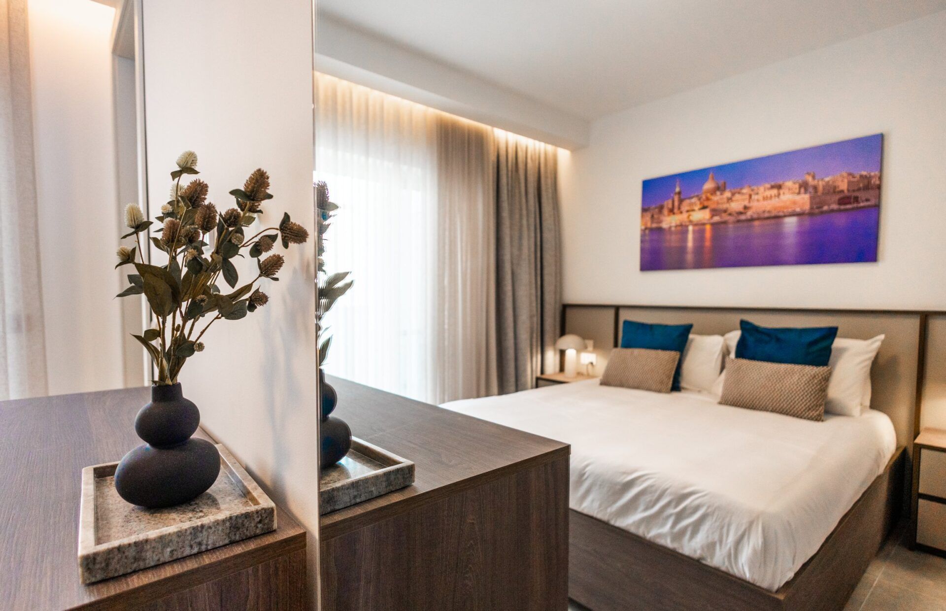 Una habitación de hotel con una cama, una mesita de noche y un cuadro de paisaje urbano en la pared.