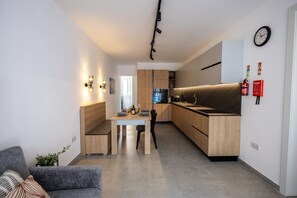 Una cuina moderna amb armaris de fusta, una zona de menjador amb taula i caires, i un rellotge a la paret.