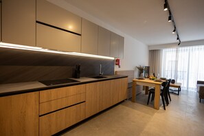 A modern kitchen with wooden cabinets, a black countertop, and a dining area with a table and chairs. - Sunny Apartment, Cozy Comfort in Style (Msida)