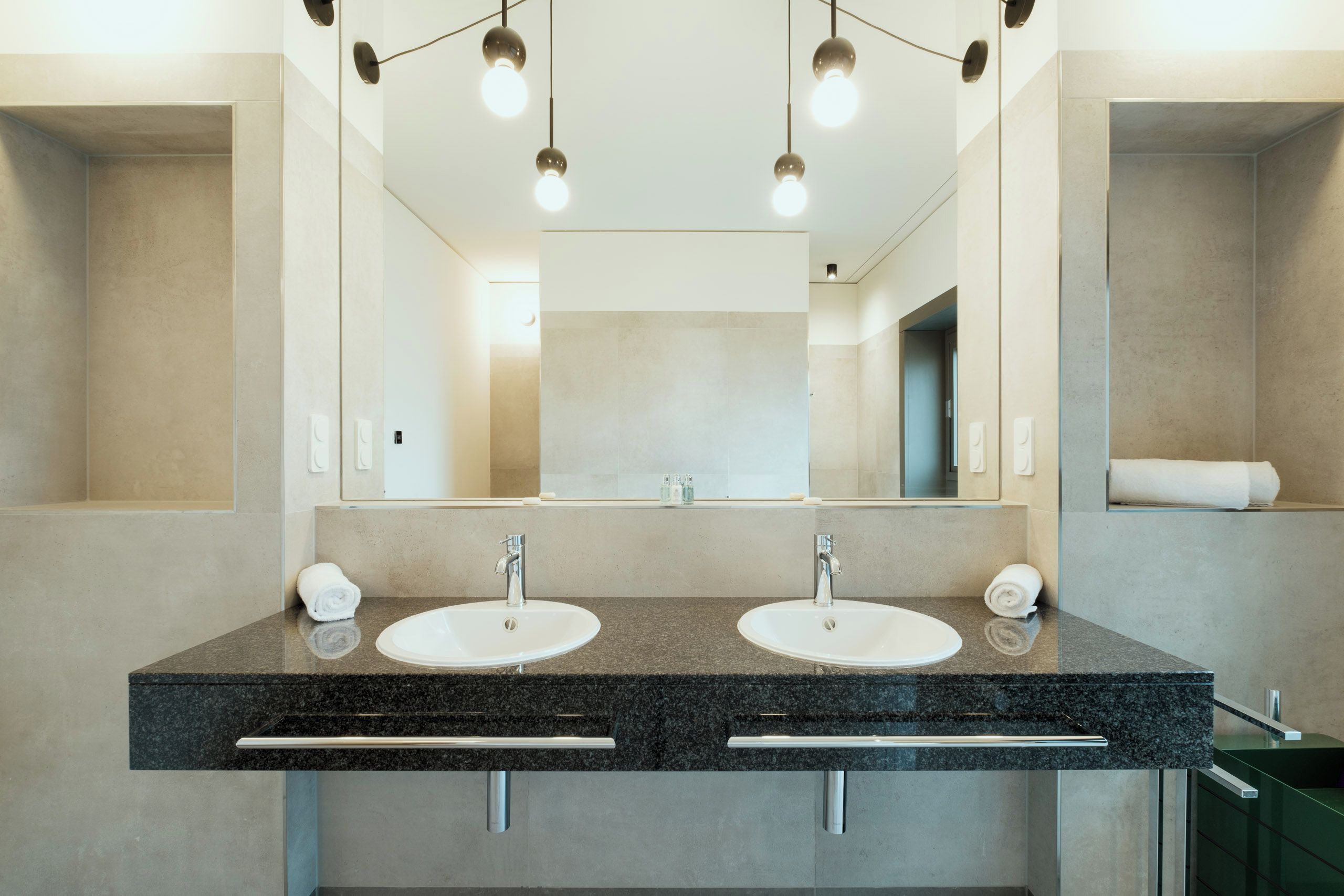 Un baño moderno con dos lavamanos, un espejo grande e iluminación colgante.