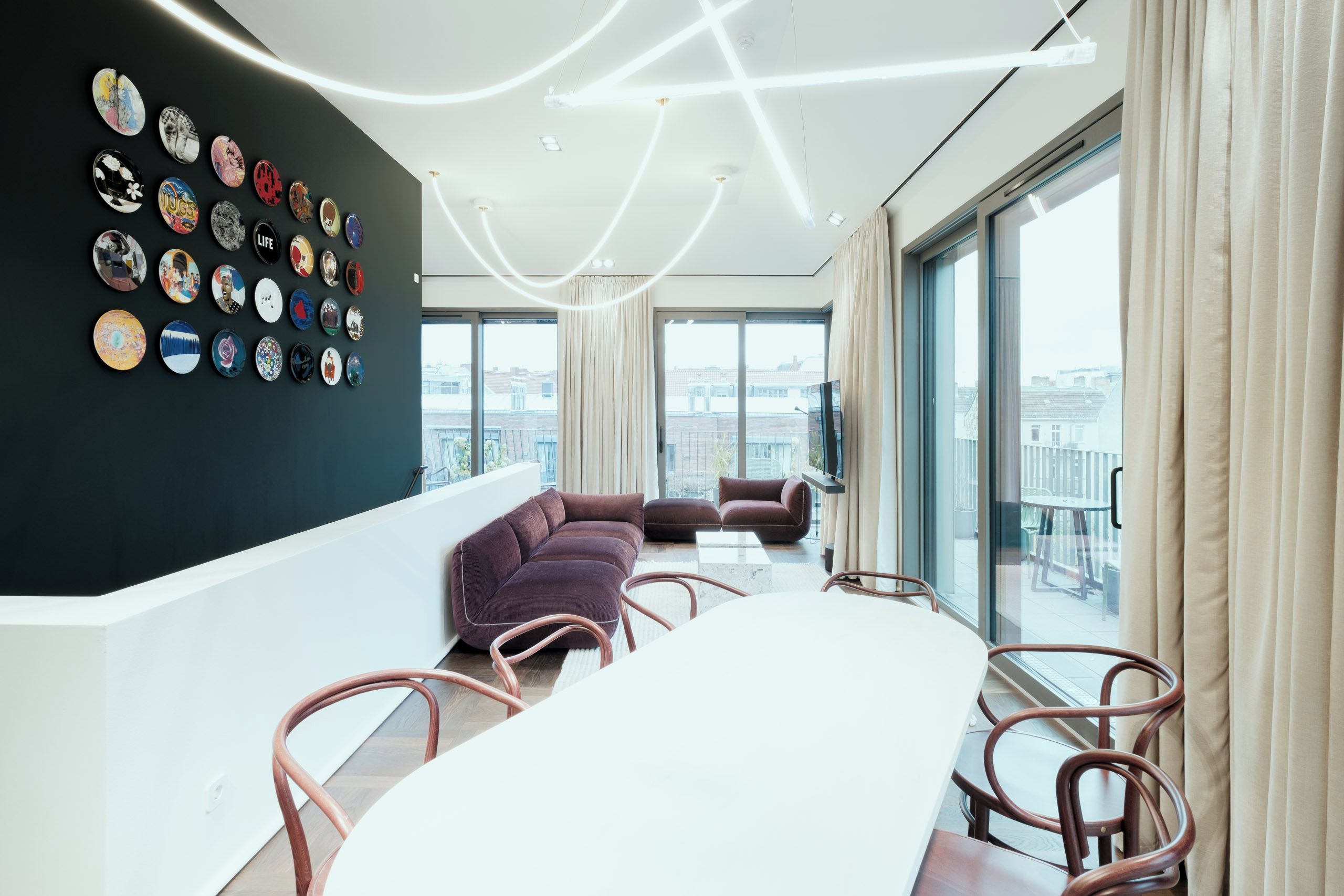 A modern living room with a large white table, a purple sofa, and a wall decorated with various circular objects.