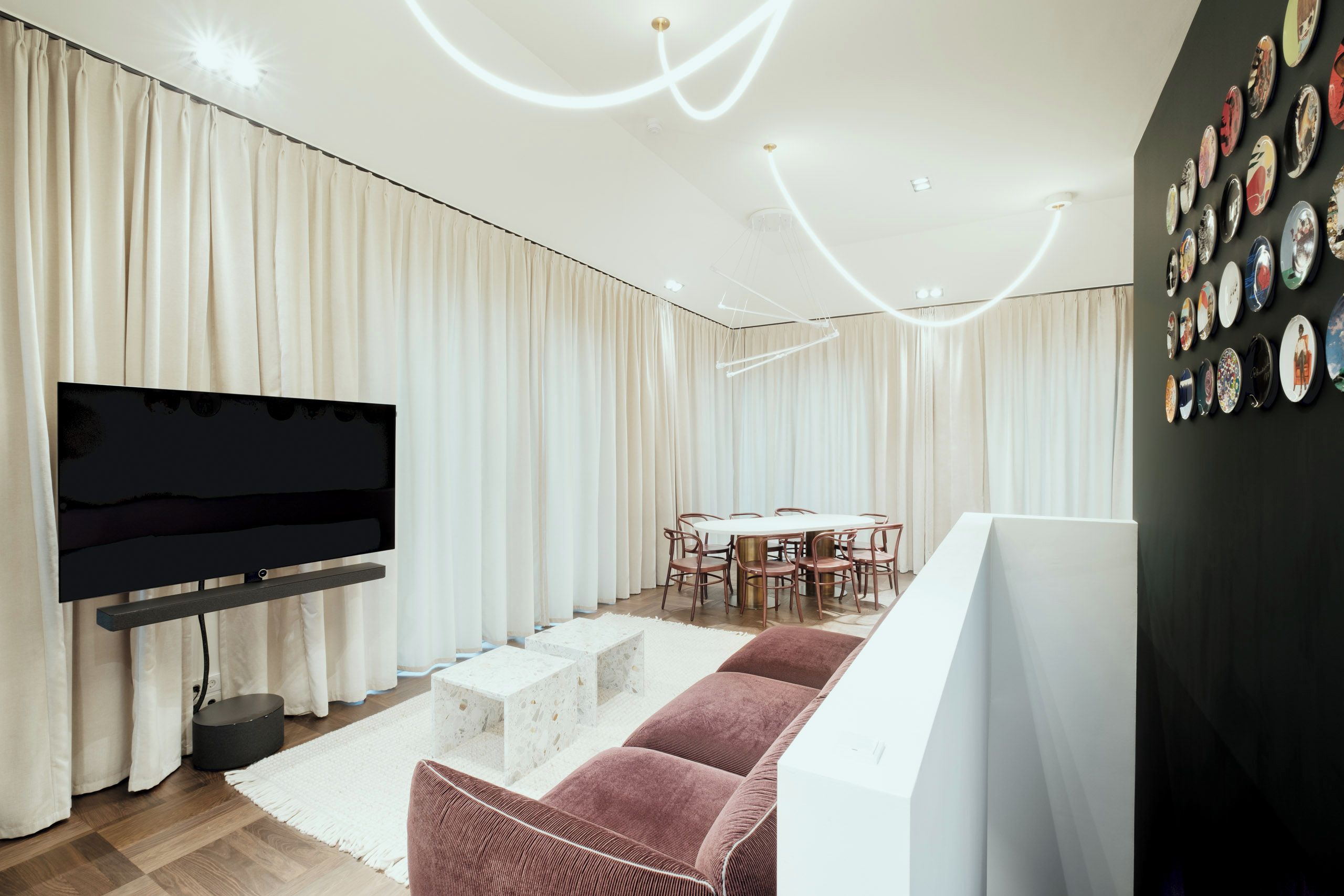 A modern living room with a flat-screen TV, a round dining table with chairs, and a wall with decorative plates.