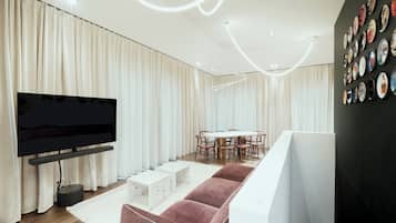 Una sala de estar moderna con un televisor de pantalla plana, una mesa de comedor redonda con sillas y una pared decorada con platos.