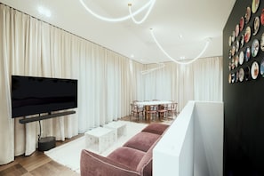 En moderne stue med et fladskærms-tv, et rundt spisebord med stole, og en væg med dekorative tallerkener.