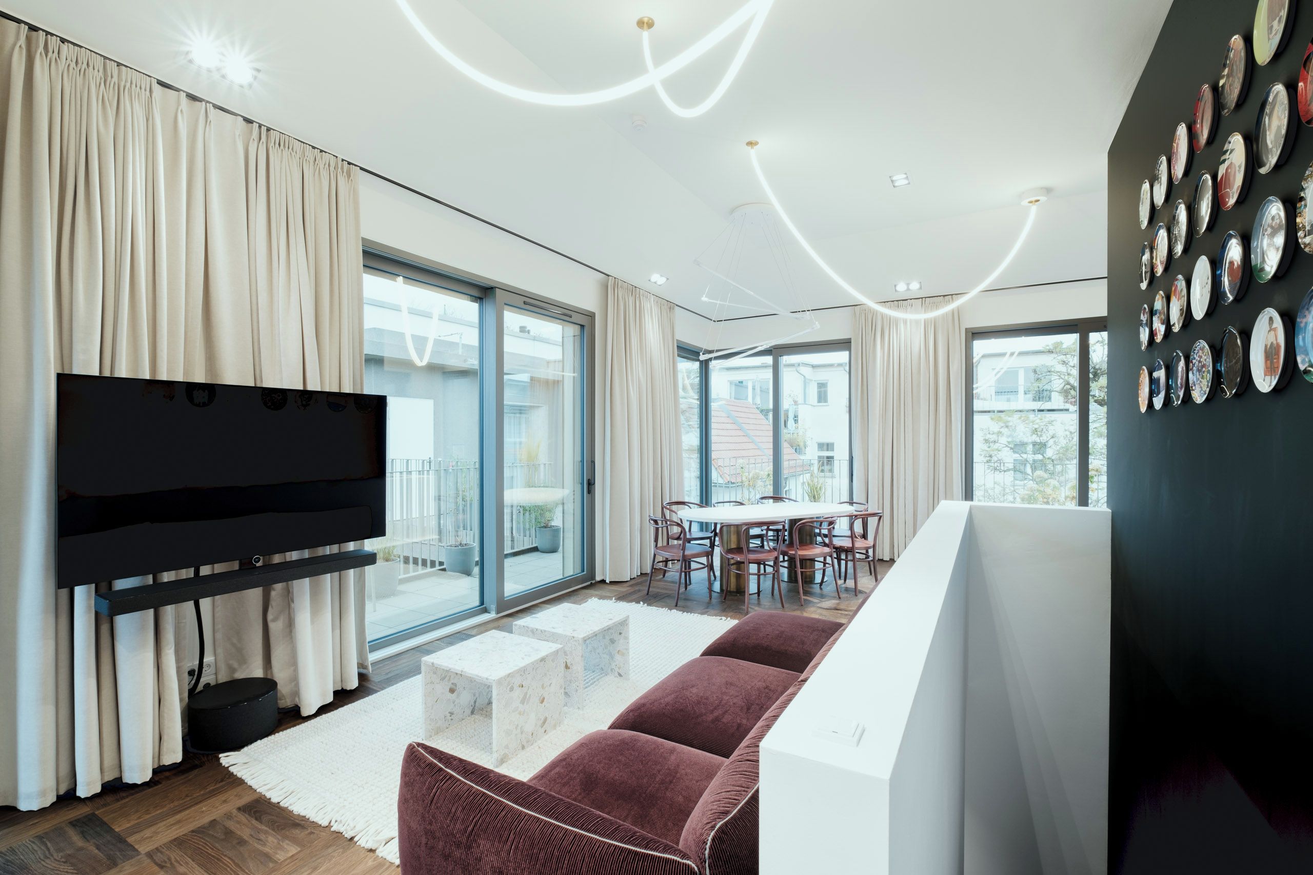 Una sala de estar moderna con un televisor de pantalla plana, un sofá, una mesa de comedor con sillas y una pared con espejos circulares.
