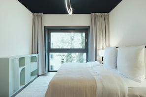Ein modernes Schlafzimmer mit großem Fenster, einem Bett mit weißer Bettwäsche und einem weißen Kleiderschrank.