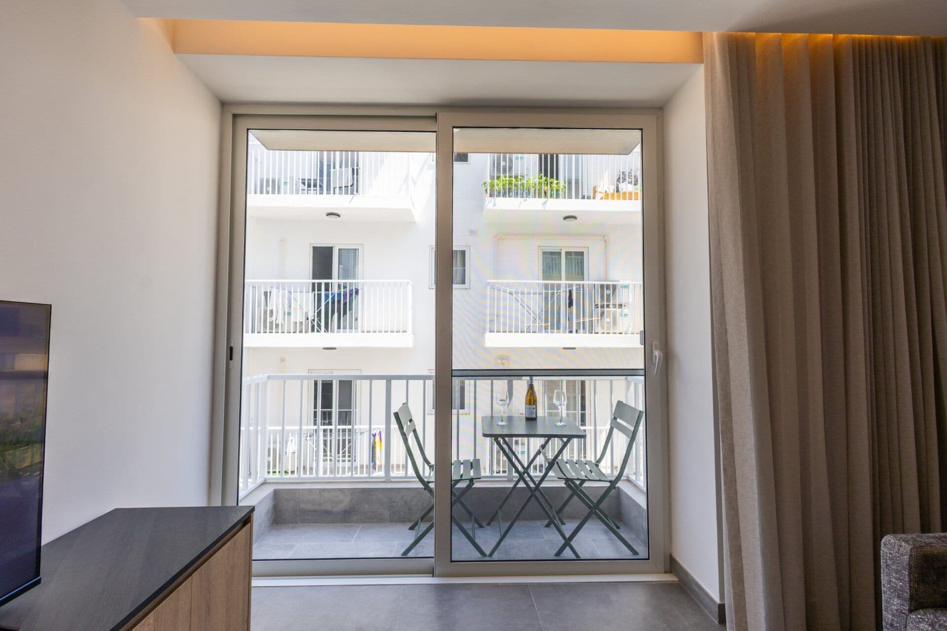 A modern apartment with a balcony, a dining table, and a TV on a cabinet.