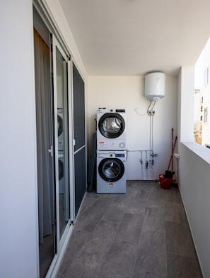 A laundry room with a stacked washer and dryer, a water heater, and a red mop bucket. - Spacious 1 Bedroom With Balcony (Msida)