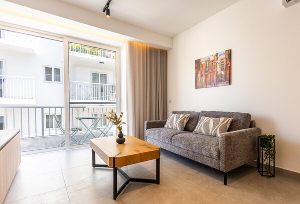 A modern living room with a grey sofa, a wooden coffee table, and a painting on the wall. - Spacious 1 Bedroom With Balcony (Msida)