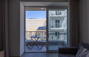 A modern apartment with a large sliding glass door leading to a balcony with a table and chairs, solar panels, and a view of neighboring buildings. - Comfortable 1BR Flat With Balcony (Msida)