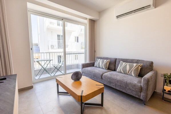 Un salon moderne avec un canapé gris, une table basse en bois et un balcon doté d’une porte vitrée.