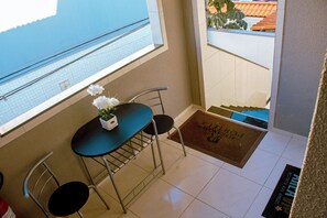 A small balcony with a table and chairs, a potted plant, and a view of a building with a tiled roof. - Fully furnished apartment near the beach, in the central area of ​​Fortaleza. (Fortaleza)