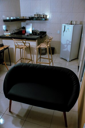 A kitchen with a black sofa, wooden chairs, a refrigerator, and a countertop with kitchenware. - Fully furnished apartment near the beach, in the central area of ​​Fortaleza. (Fortaleza)