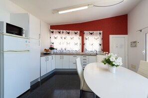 Ett modernt kök med vita skåp, en mikrovågsugn och en matplats med ett vitt bord och stolar.