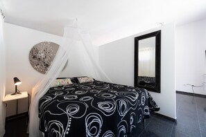 Ett sovrum med en säng, ett sängbord med en lampa, en spegel som hänger på väggen och en dekorativ väggdekoration.