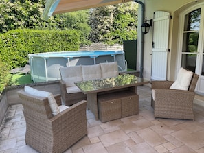 Un patio al aire libre con mobiliario de mimbre, una mesa con cubierta de vidrio y una piscina al fondo.
