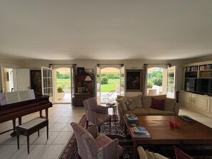 A spacious living room with a piano, a sofa set, a coffee table, and a bookshelf.