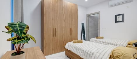 A modern bedroom with a wooden wardrobe, a bed with a patterned bedspread, a potted plant, and an air conditioning unit.