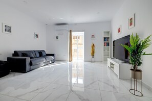 A modern living room with a sofa, a flat-screen TV, a bookshelf, and a potted plant. - Modern Family Holiday Retreat in Gzira (Gzira)