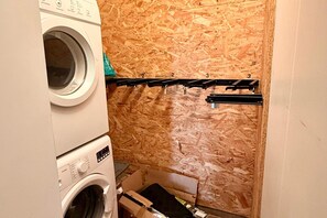A laundry area with stacked washing machines and a drying rack against a wooden wall. - Alpine holiday home with balcony (Mont-Dore)