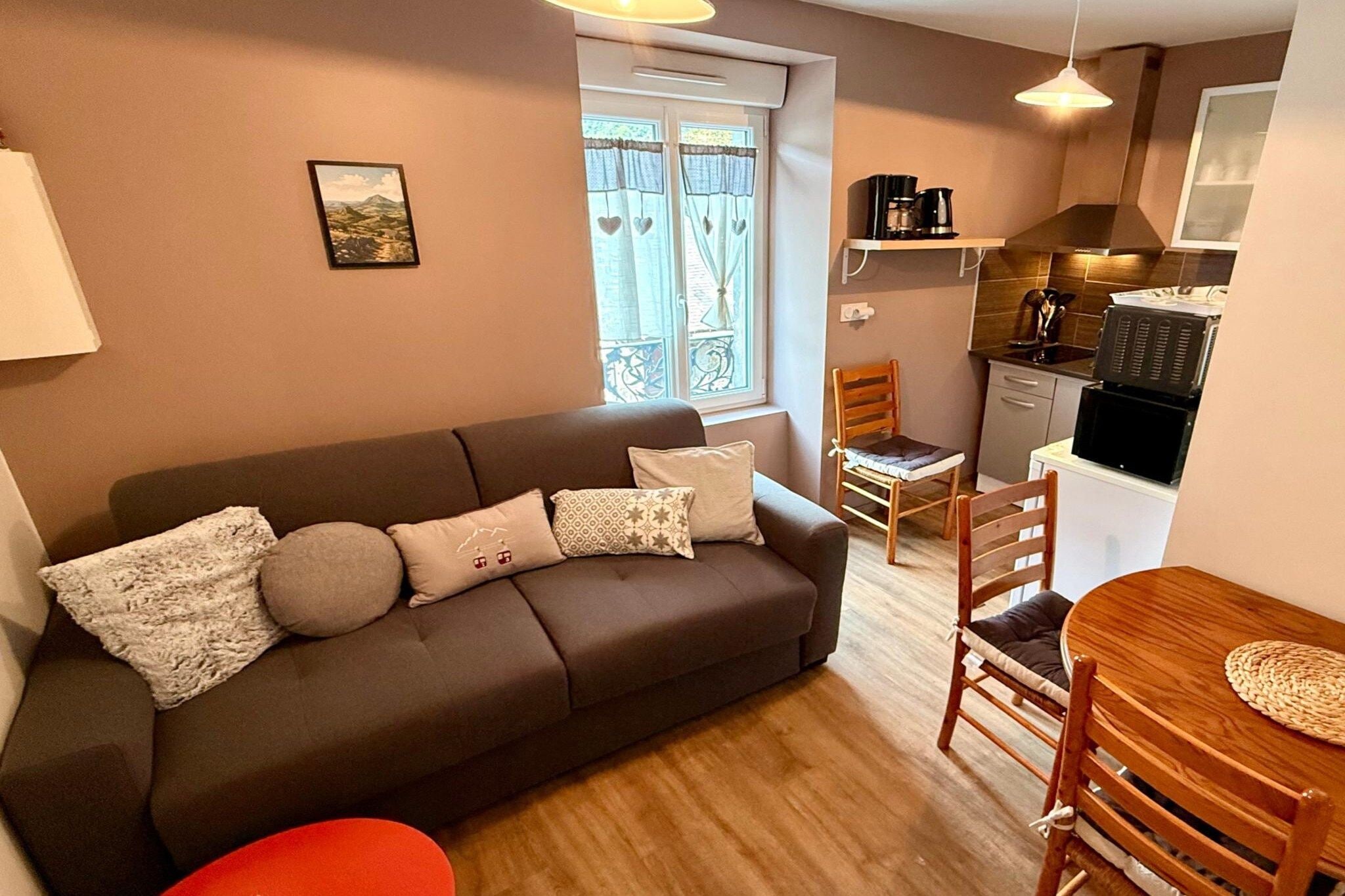 A cozy living area with a sofa, a dining table, and chairs. There is a kitchen area with a stove and a coffee maker.
