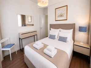 A hotel room with a bed, a desk, a chair, and a bedside table with a lamp. - Gardens Coastal Apt by TrulyCyprus (Lemesos)